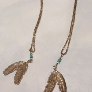 Ladies silver tone necklace with blue beads at the end, towards the feather pend